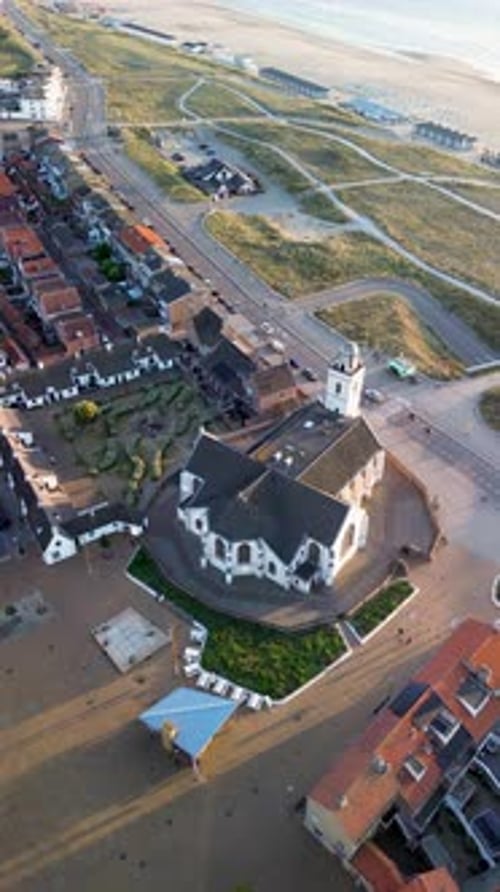 Aerial view of a coastal town with a white church, red-roofed homes, and a landscaped courtyard
