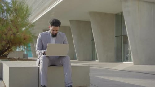 Man in Suit Uses Laptop Outside Office Building