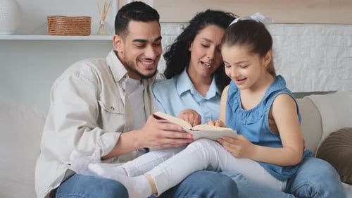 Hispanic Multiethnic Family Sitting on Couch Sofa Mother Father and Child Girl Reading Book