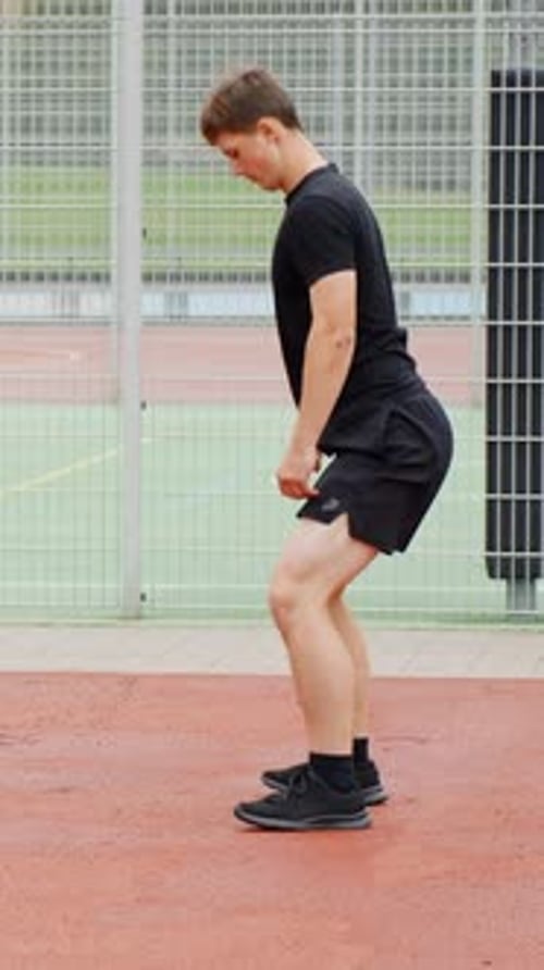 Young man performing bodyweight squats outdoors, engaging in a fitness workout on a sports court