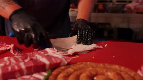 Butcher with black gloves cutting raw lamb loin chopsin the kitchen.