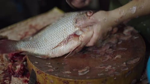 Fish Seller Cleaning and Removing the Skin From Fresh Fish on a Round Board with a Large Knife at a