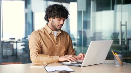 A young employee using typing on laptop while sitting at the work desk at workplace in modern office