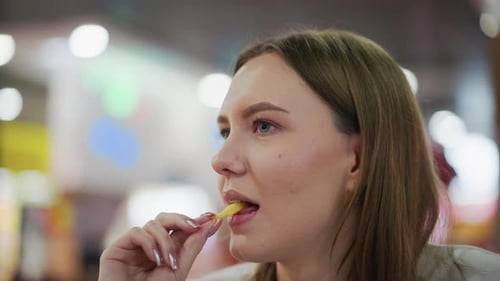 Lady Eating Fries in Shopping Mall with Colorful Lights Background