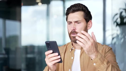 Concerned Man Holding Phone in Modern Workplace