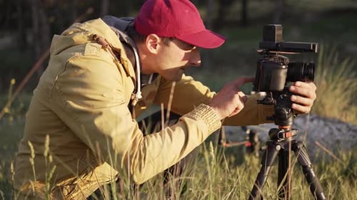 Man Adjusting Camera on Tripod in Field