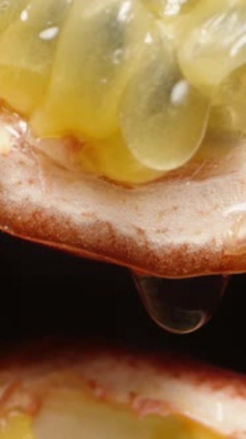 Vertical video. Macro slider shot of a passion fruit cut in half, with juice dripping down from one
