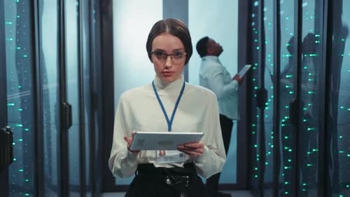 A Woman is in a Data Center Carefully Analyzing and Managing Information Displayed on Her Tablet