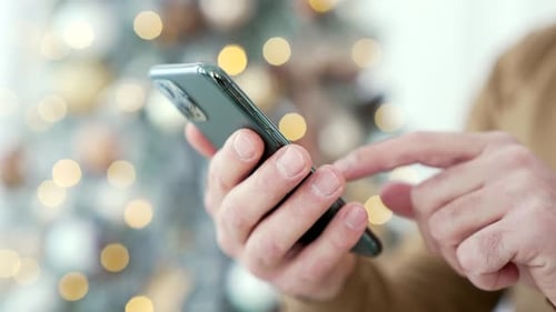 Close up. A man's hand holds a smartphone at home during winter New Year Xmas holidays