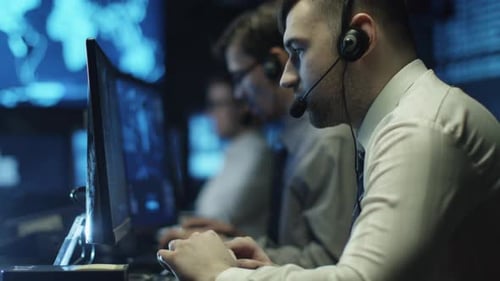 Two IT programmers are working on computer in headset in a dark office room filled with display scr