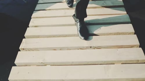 Pés de homem em sapatos pretos andando em uma ponte de madeira sobre a água