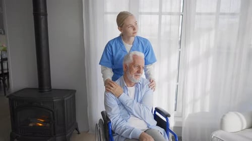 Woman Comforts Elderly Man in Wheelchair Indoors