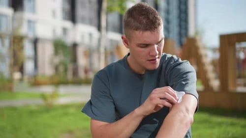 Young Adult Applying Bandage to Arm in Park