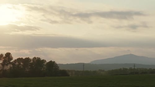 Sunset timelapse of a green land with background mountains in a foggy day. The sun first disappears