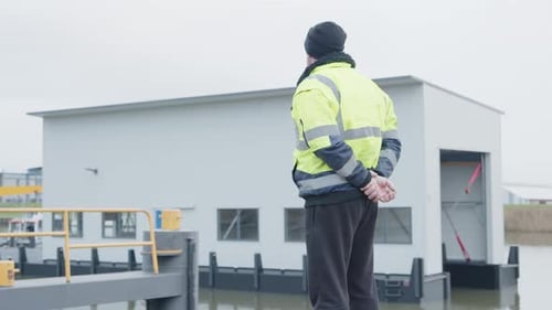 seaman with clasped hands looking over a ship in the harbour.