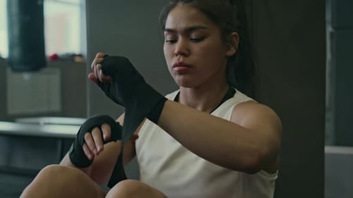 Hispanic Female Combat Fighter Wrapping Hands for Training at Gym