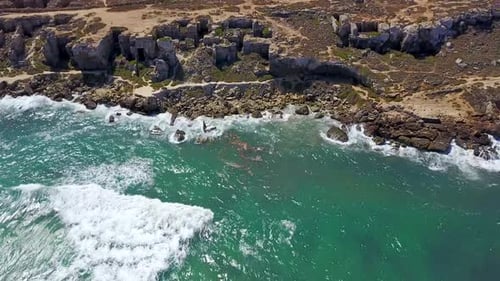 drone shot flying over waves crashing on coast rocky cliffs. Mediterranean dry landscape on the back