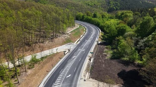 An aerial view shows a modern winding highway with fresh asphalt and clear markings snaking through