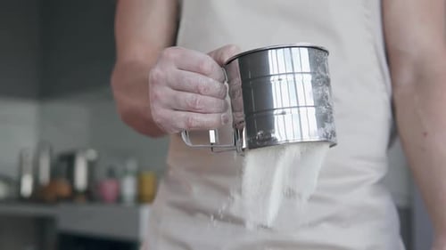 Person Sifting Flour in Kitchen with Metal Sifter