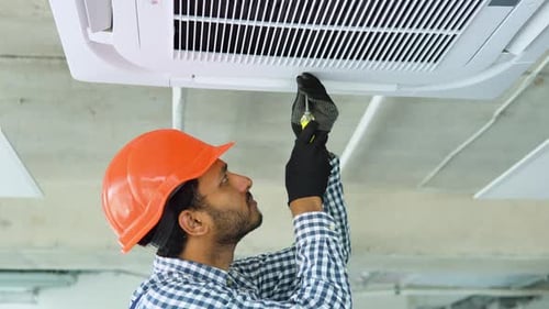 HVAC Worker Repairs Air Conditioner in Office