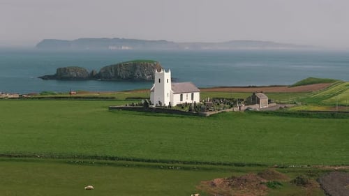 Aerial Pan Down of Coastal White Church with Sheep in Northern Ireland
