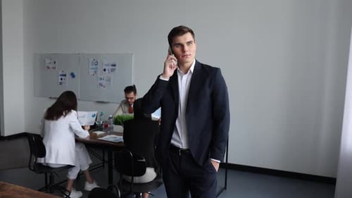 Project Manager Speaks on a Mobile Phone on the Background of the Office By Employees at Workplaces