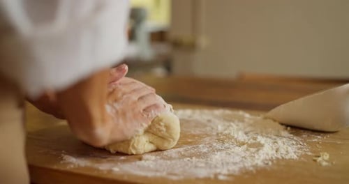 Closeup a Girl in a White Shirt and Beige Apron Sprinkles Flour on Dough While Kneading and