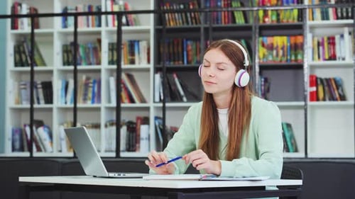 Kaukasisches Schulmädchen mit Kopfhörern träumt in der Bibliothek