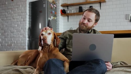 Man Petting Dog While Using Laptop at Home