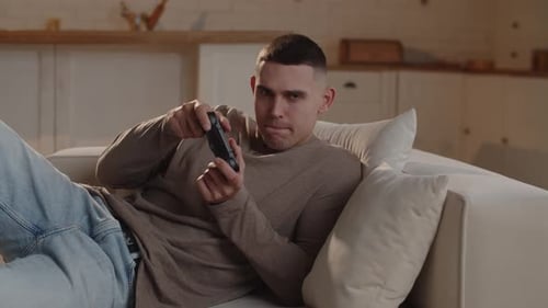 Closeup Shot of a Man Lying on a Couch with a Gamepad in His Hands Who is Trying to Pass a Difficult
