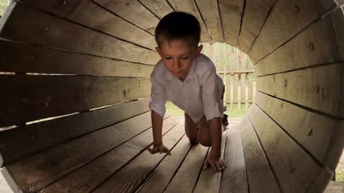 Happy smiling boy crawling through wooden tube at summer extreme adventure park