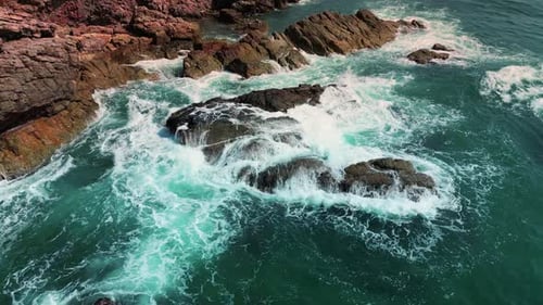 Top View Colorful Waters of the Ocean Swirl Around the Rocky and Scenic Coastline Sea Waves Breaking