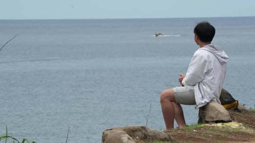Young Man Contemplating Sits Near Seacoast. Static Shot