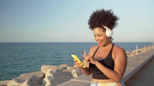 Video of Curve Hispanic woman in sportswear and headphones enjoying music and dancing on pier