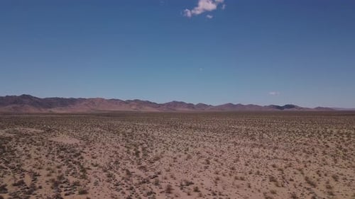 Arizona aerial over an empty desert towards a mountain range with scrub land in the foreground - Dro