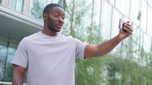 African American Man Holding Smartphone Having Video Chat on Urban Street in City Guy Blogger