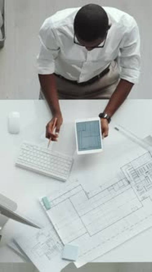 Schwarzer männlicher Architekt arbeitet mit digitalem Tablet an Bauplan
