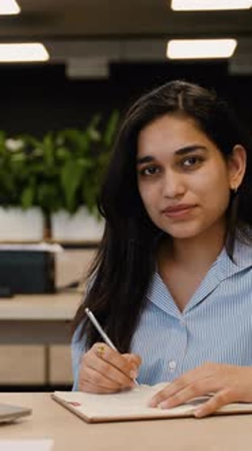 Woman Writes in Notebook at Desk in Office