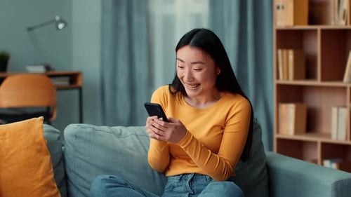 Excited Woman Using Phone on Couch at Home