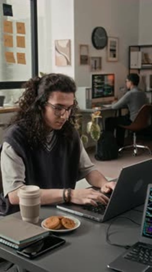 Vertical de un ingeniero de software masculino de la generación Z codificando en una computadora portátil en un escritorio de madera