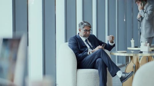 Senior Businessman Drinking Coffee and Using Smartphone in Cafe