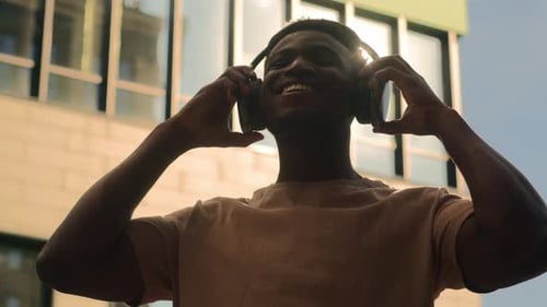 Man Puts On Headphones in City Sunlight