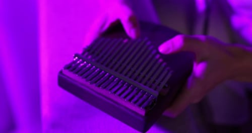 Woman playing kalimba in pink light at home, closeup. Camera moving right
