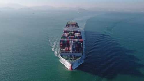 Aerial front view of a loaded container cargo vessel traveling over ocean.