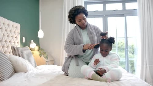 Woman Brushing Child's Hair on Bed