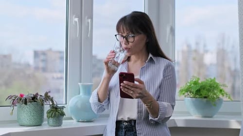 Woman Using Phone and Drinking Water by Window
