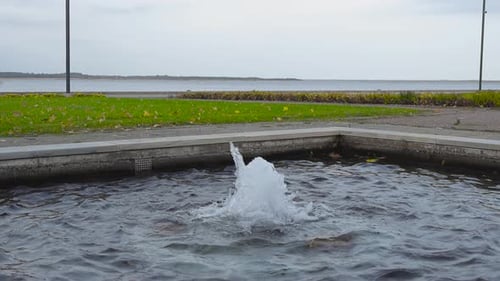 Small water fountain shooting up water in slow motion at Haapsalu promenade by the sea at cloudy day