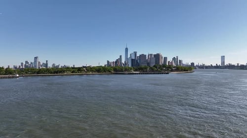 A low altitude, aerial view of lower Manhattan from New York Harbor on a sunny day with blue skies.