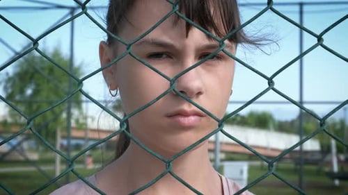 Teen Behind Chain Link Fence Looks Serious