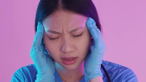 Distressed Medical Worker Rubbing Temples with Gloved Hands
